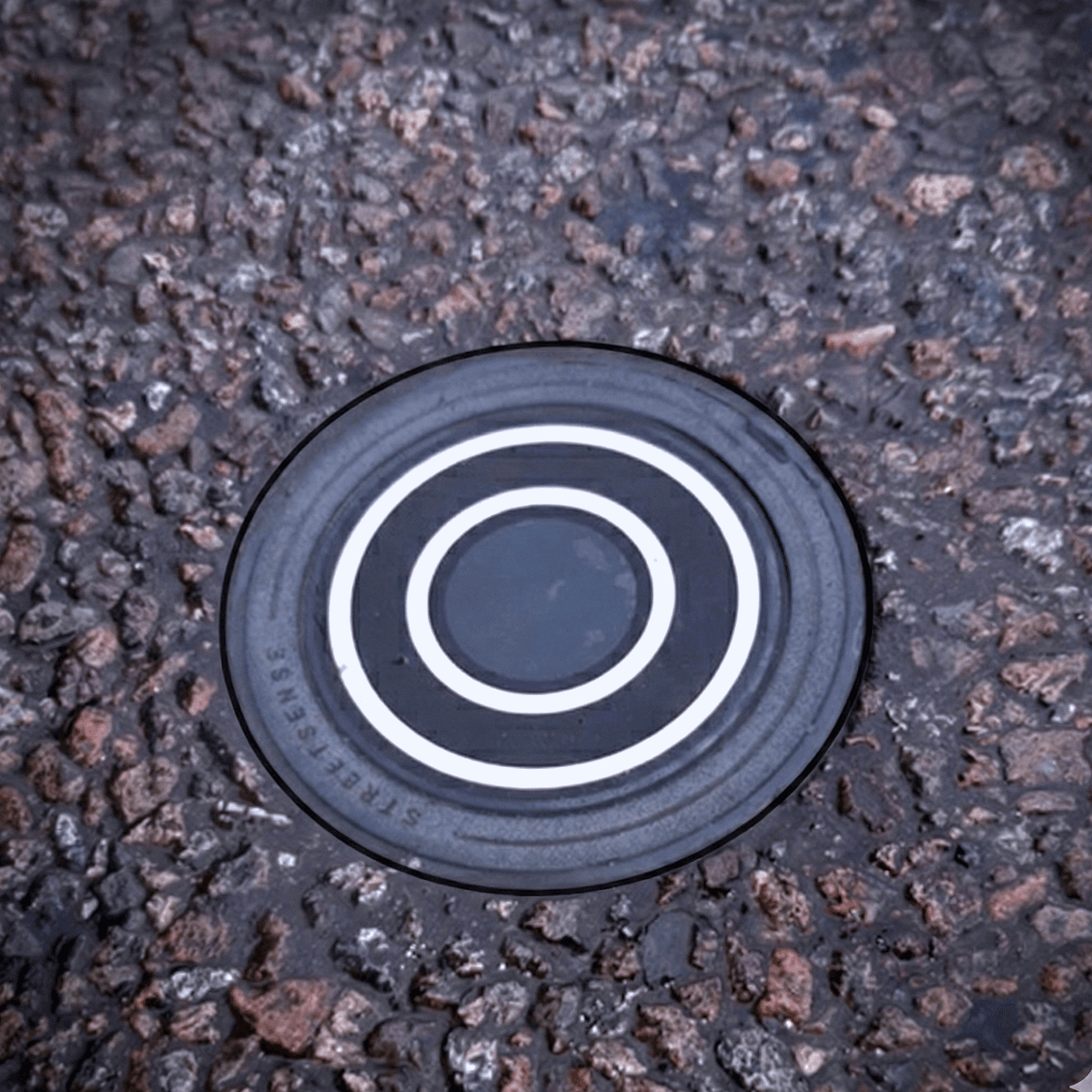 StreetSense IoT sensor installed flush in a road surface, showing its concentric ring design embedded in asphalt